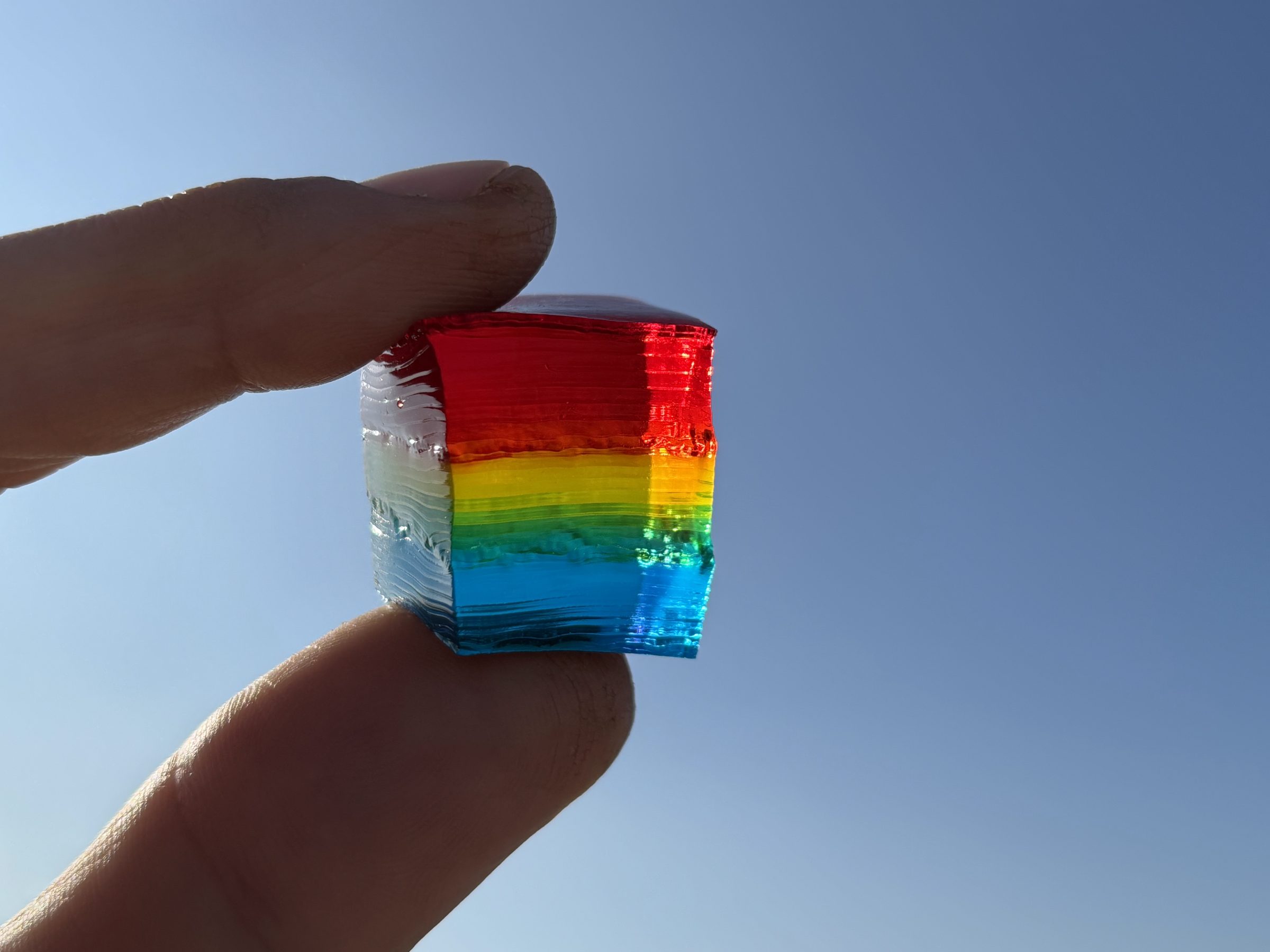A rainbow jello cube held up against a blue sky
